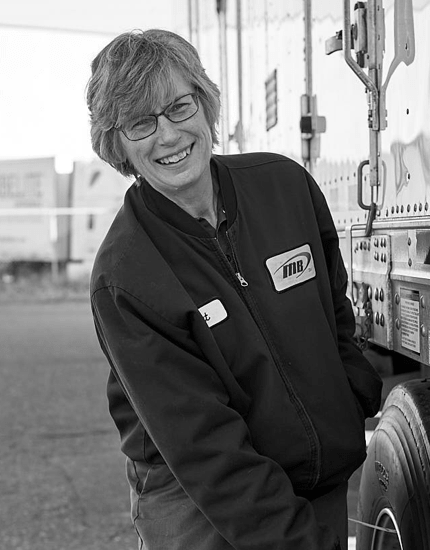 A Reyes Holdings team member from the Martin Brower division, smiling and standing next to an 18-wheeler truck's roll up door.